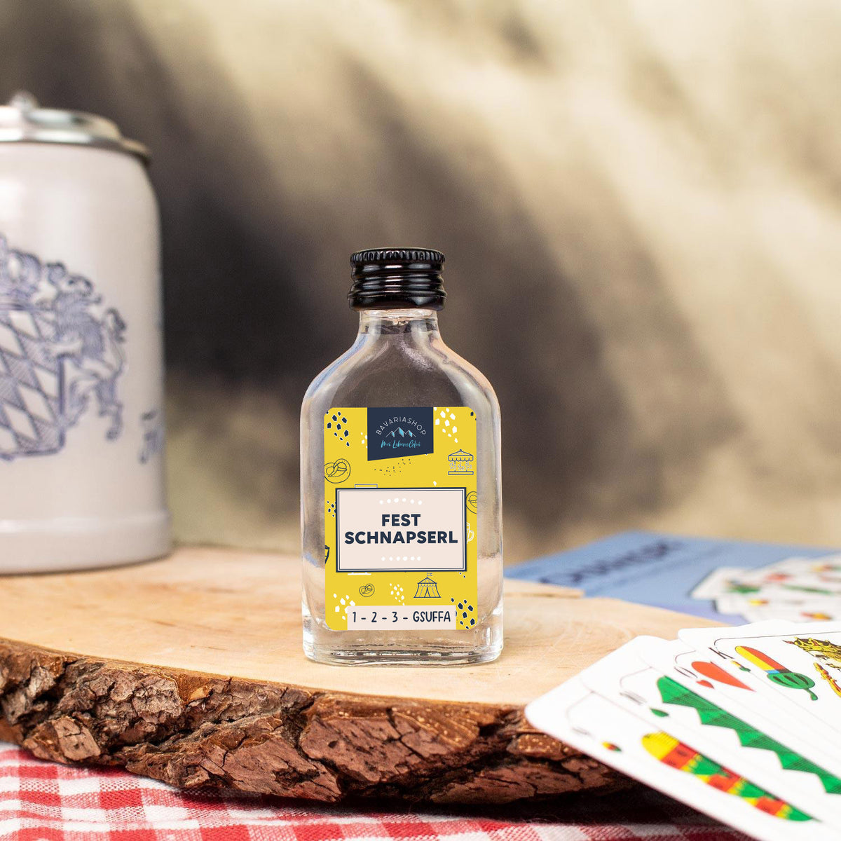 Fest Schnapserl 2cl Miniaturflasche mit gelbem Etikett auf Holzbrett, umgeben von Spielkarten und Bierkrug.