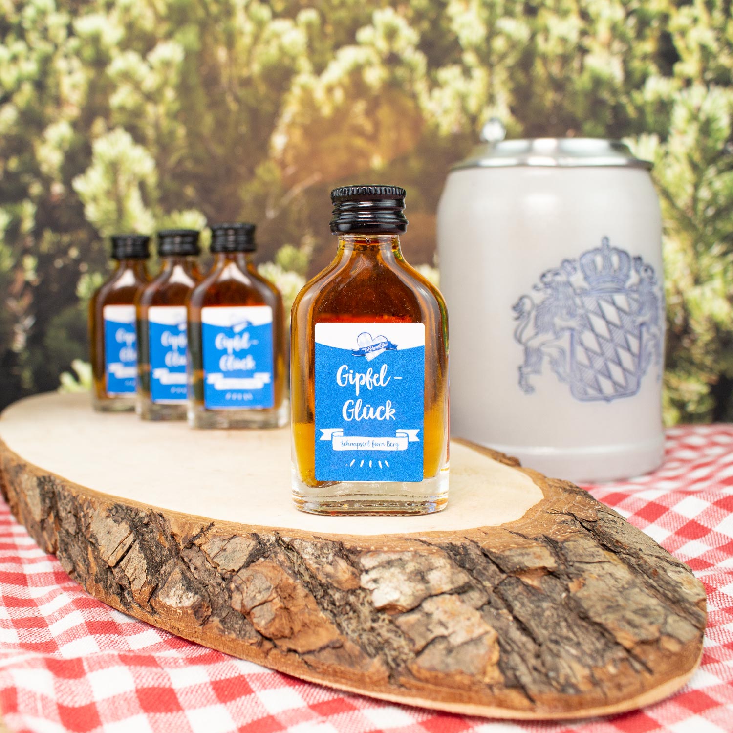 Vier kleine Schnapserl Gipfel-Glück Flaschen auf Holzbrett, daneben Bierkrug, bayerisches Design.