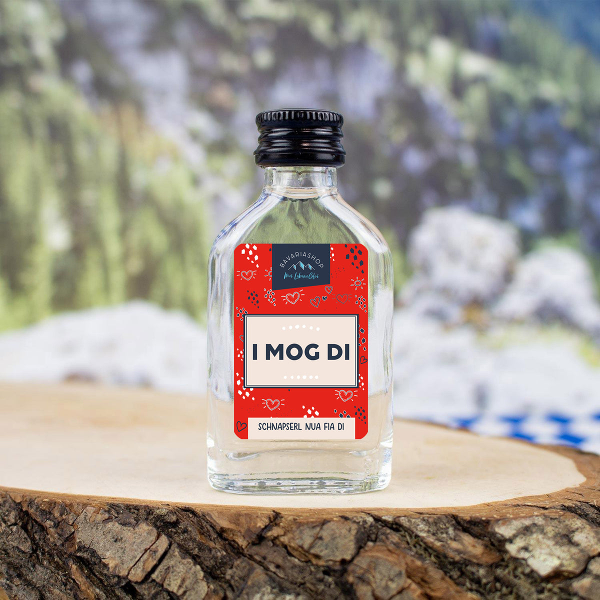 Kleines Schnapserl "I mog di" mit rotem Etikett und weißer Aufschrift auf Holzscheibe, als Geschenkidee.