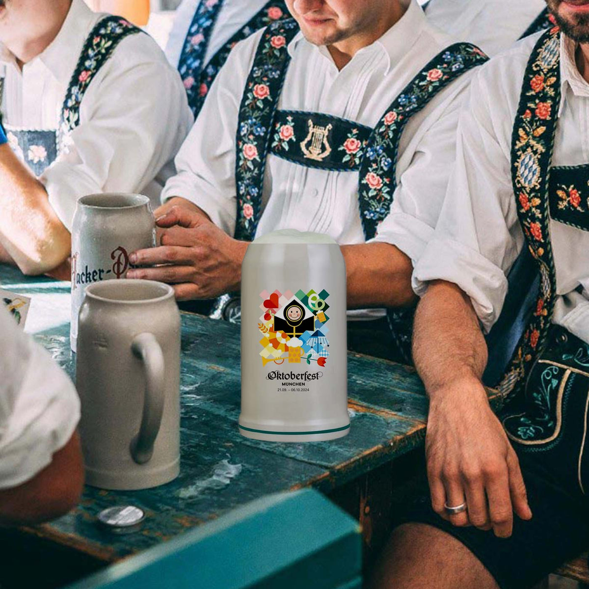 Offizieller Oktoberfestkrug 2024 mit bunten Motiven auf Holztisch inmitten bayerisch gekleideter Personen.