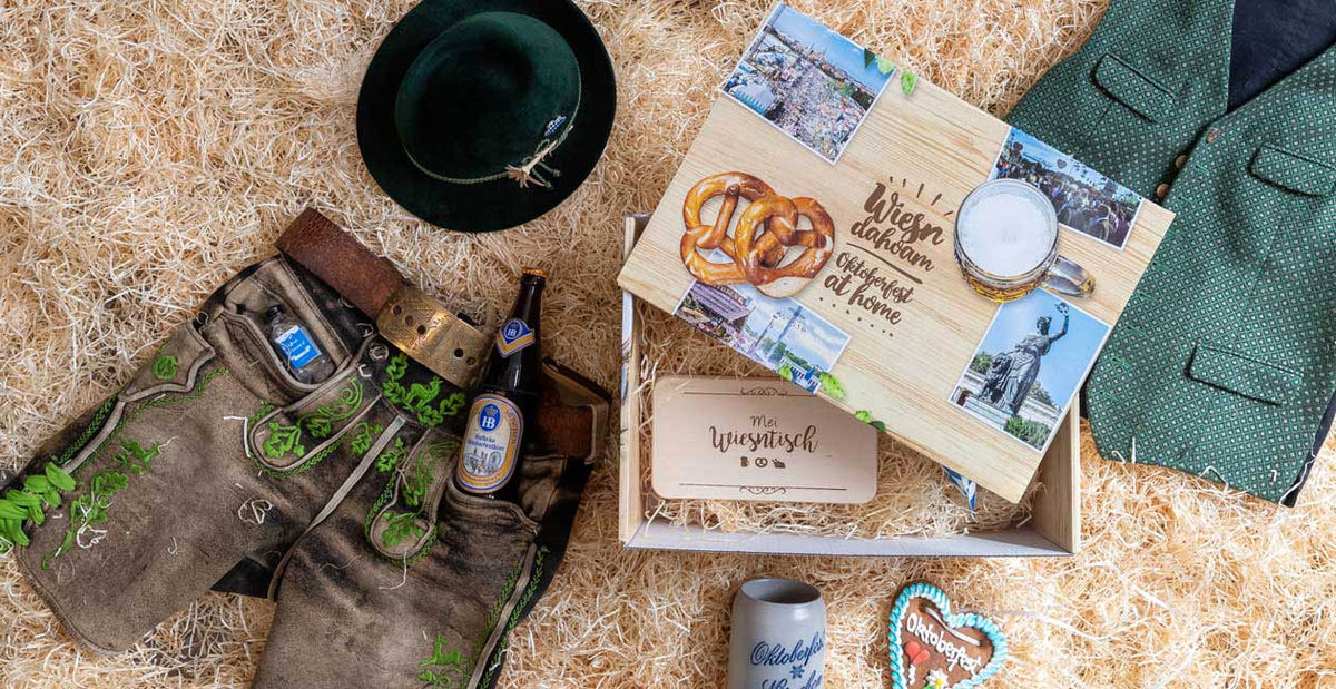 Geschenkbox mit bayerischer Tracht, Bier und Oktoberfest-Accessoires auf Heubett für bayerische Feiern.
